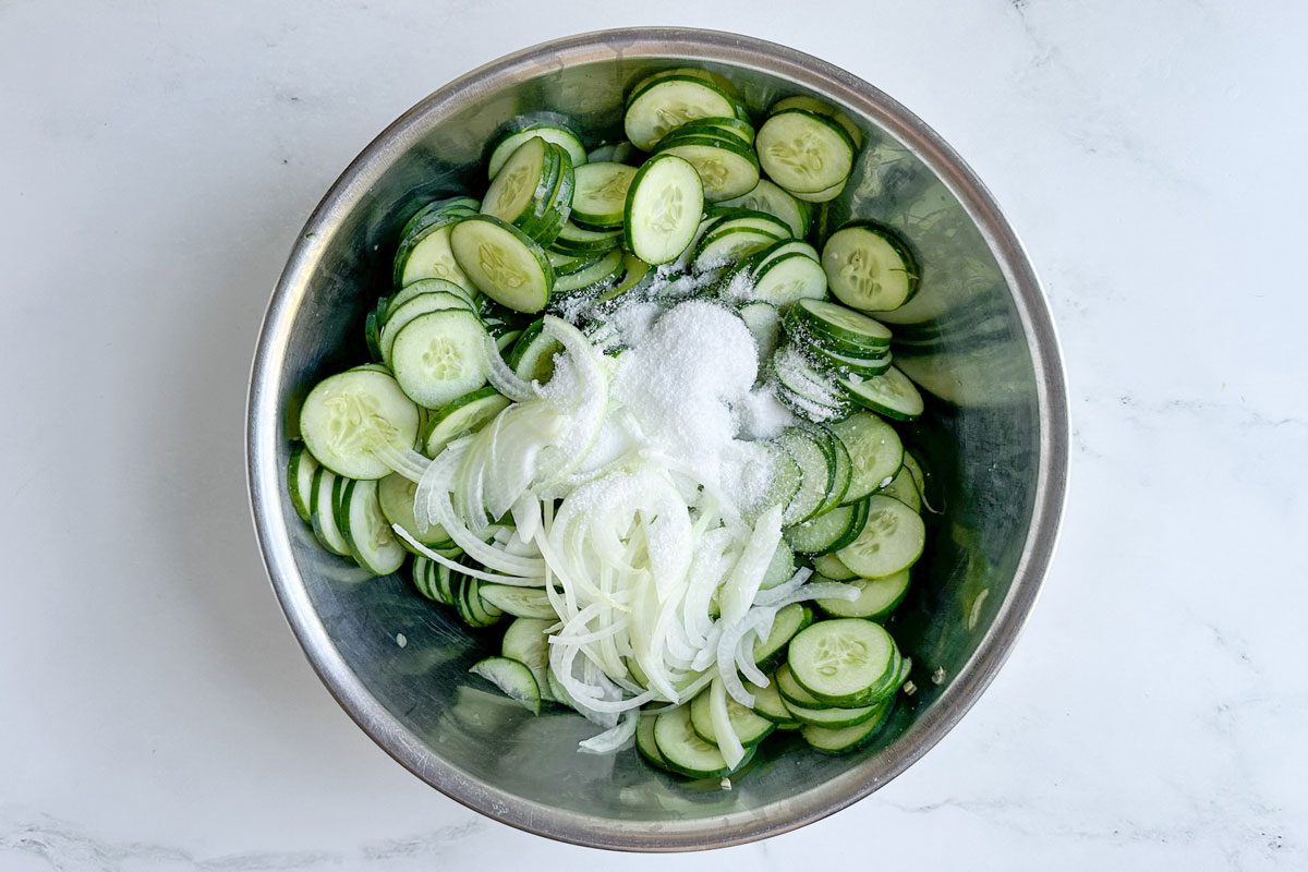Cucumbers onions and salt for Taste of Home Freezer Pickles in a metal bowl
