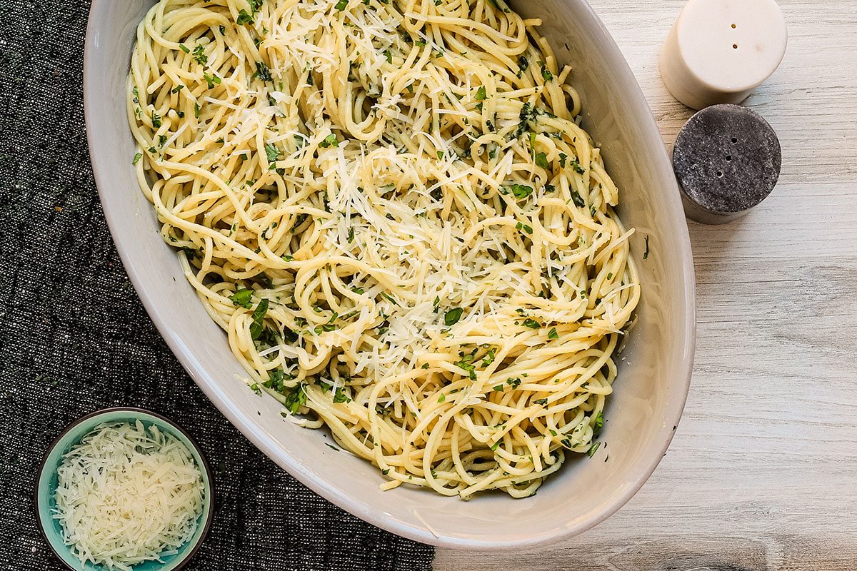 Garlic spaghetti in a serving bowl with a Parmesan cheese garnish and parsley.
