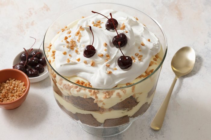 High angle view shot of Gingerbread Trifle; garnish with cherries; serving spoon; marble surface.