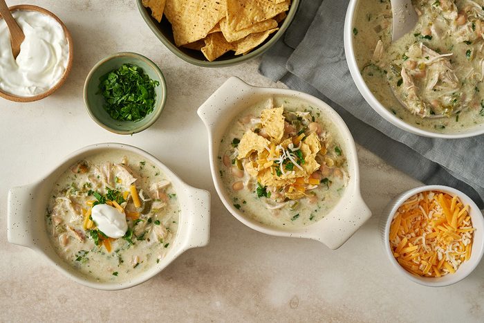 Overhead hero shot of the finished Taste of Home Green Chicken Chili, served in a bowl with toppings of shredded Colby-Monterey Jack cheese, extra sour cream, and crushed tortilla chips.