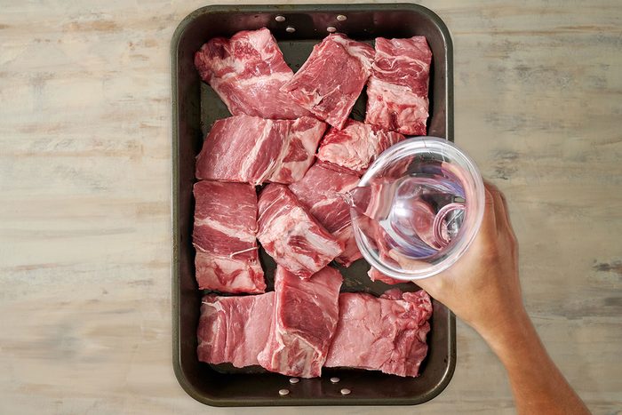 Overhead view of pork baby back ribs in a roasting pan with water poured over, covered with aluminum foil, and ready to bake for the Taste of Home Honey Garlic Ribs recipe.