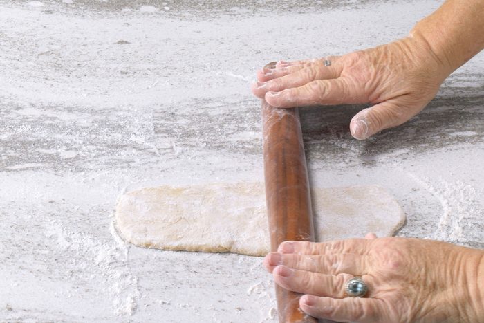 Rolling the dough using a rolling pin on a floured surface