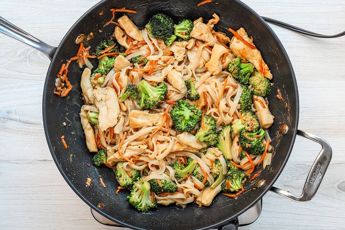Combining the stir-fried vegetables with the sauce, cooked chicken and rice noodles for peanut chicken stir-fry.