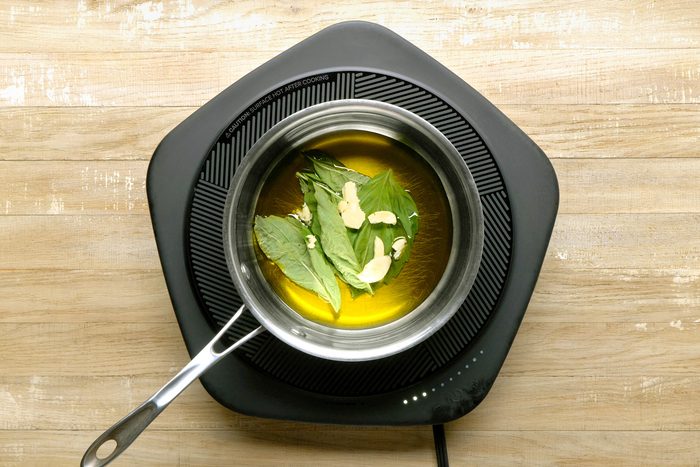 Olive oil, basil leaves, and garlic combined in a small saucepan.