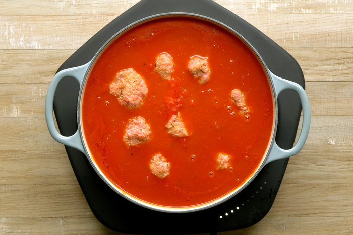 Adding raw meatballs to the simmering sauce.