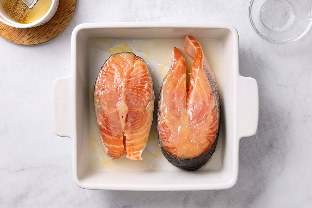 Salmon steaks in a greased baking dish, topped with melted butter and lemon juice for step two of Salmon Steak recipe for Taste of Home