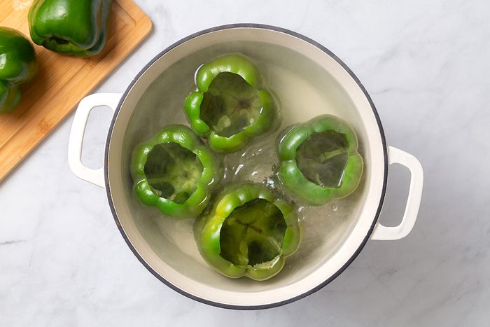 Green peppers with tops chopped off boiling in hot water in a Dutch oven for step one of Stuffed Peppers with Cheese recipe for Taste of Home
