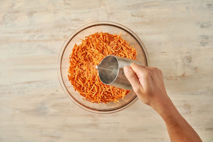 Overhead view of shredded sweet potatoes in a bowl with boiling water being poured over them for The Taste of Home Sweet Potato Fritters recipe.