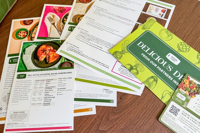 Scattered recipe cards and a "Delicious Deals" pamphlet are spread on a wooden surface. The cards feature images of meals, ingredients, and cooking instructions.