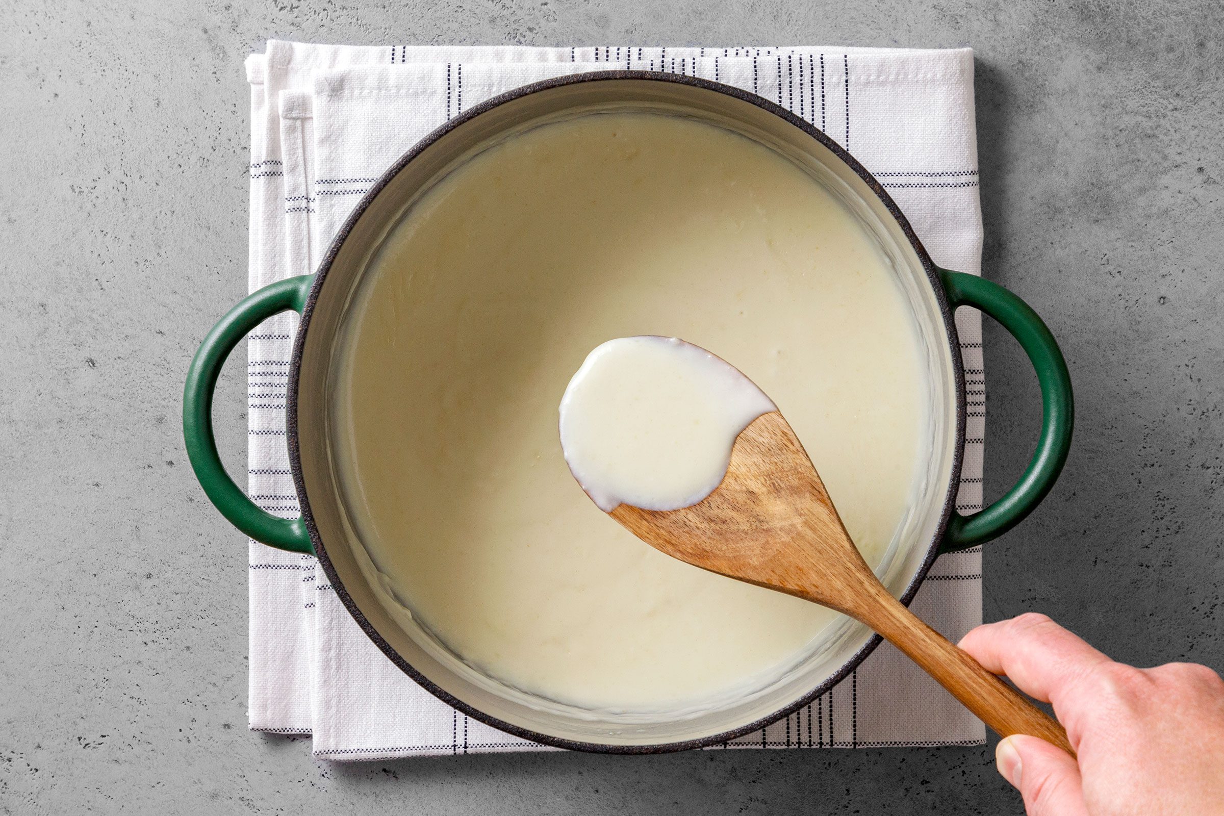 Cheese sauce in a large saucepot with a wooden ladle 
