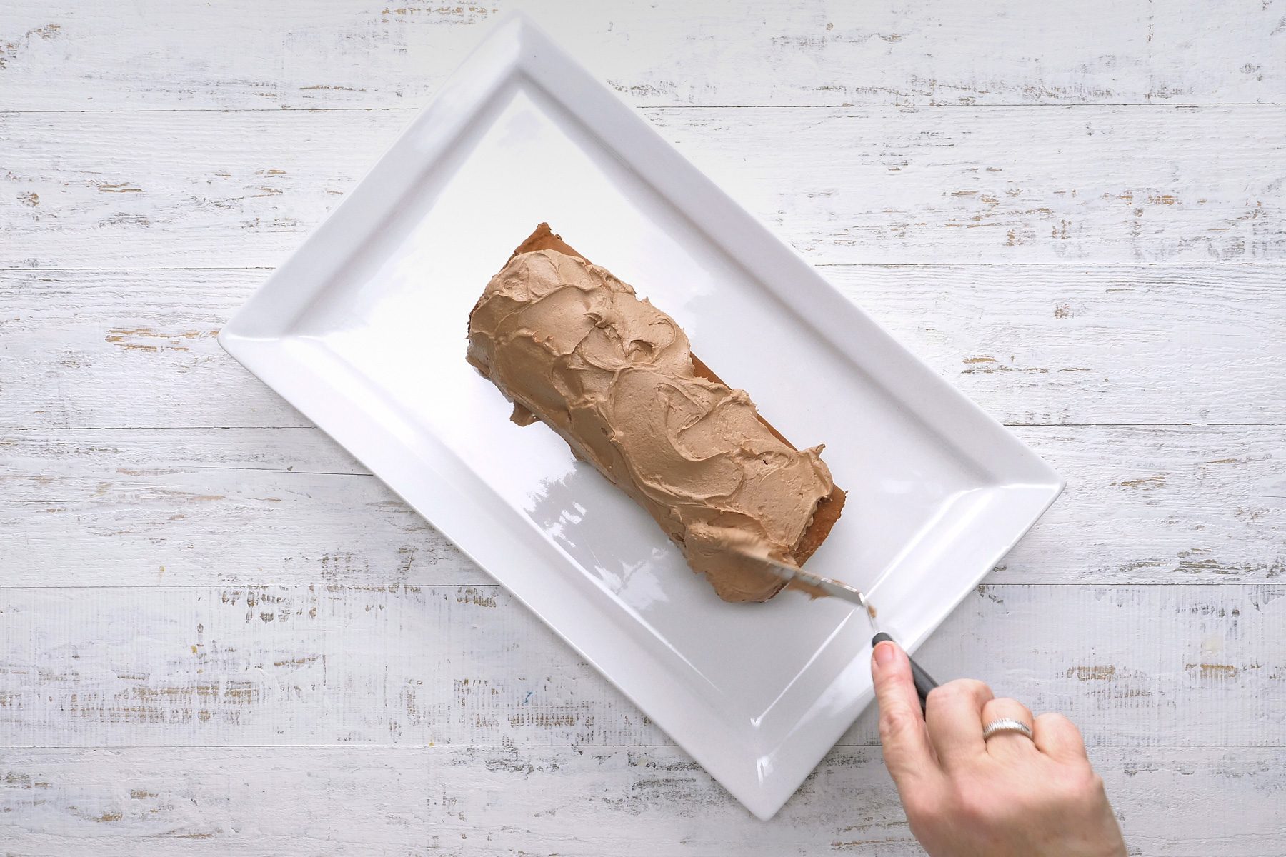 Frosting the cake with a metal spatula to create a bark-like texture.