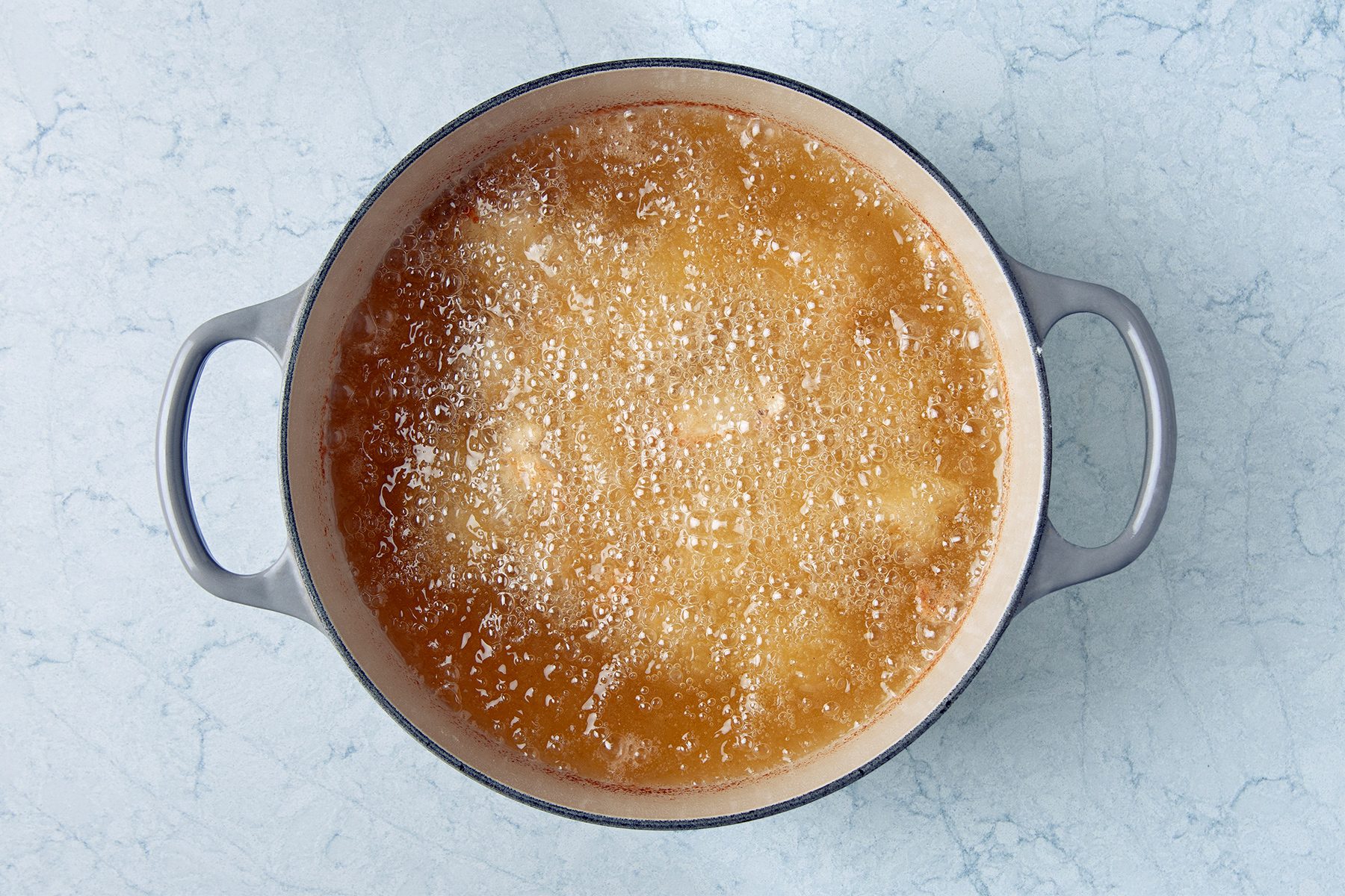 A pot filled with simmering golden-brown oil on a light blue marble surface.