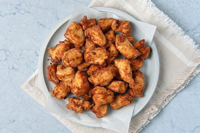 A plate of fried chicken pieces on a light-colored napkin and marble surface.