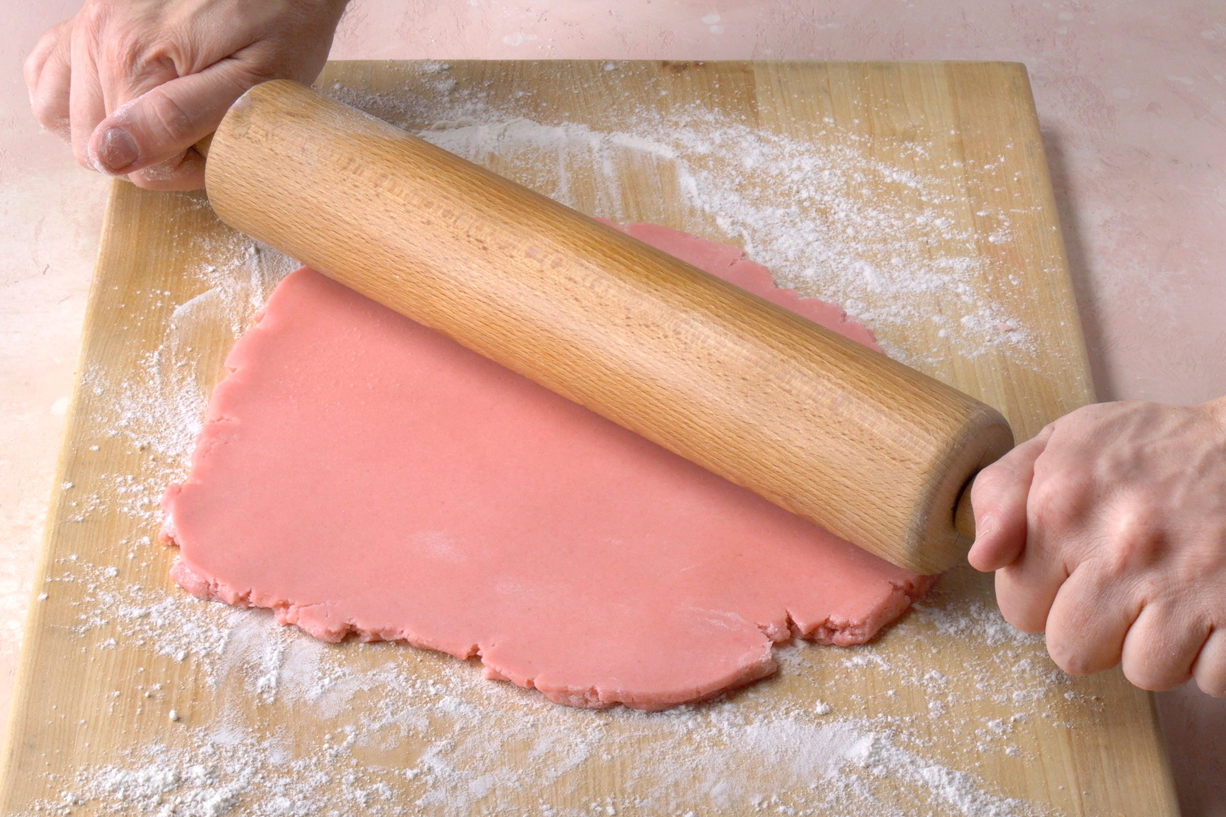 Rolling pink cookie dough on a wooden board using a rolling pin