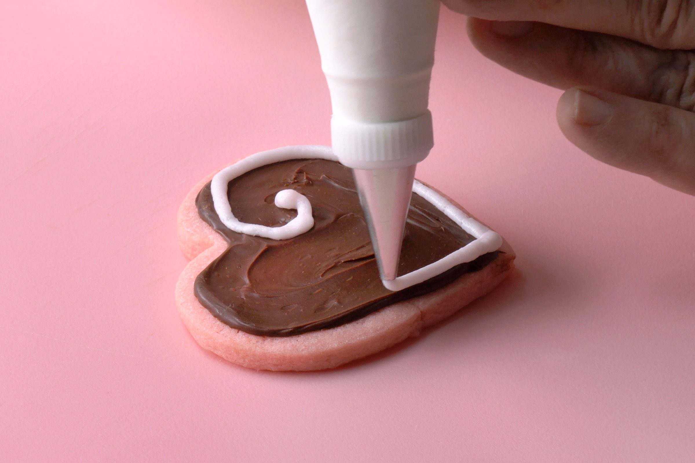 Valentines Cookies being decorated with strawberry frosting using a piping bag