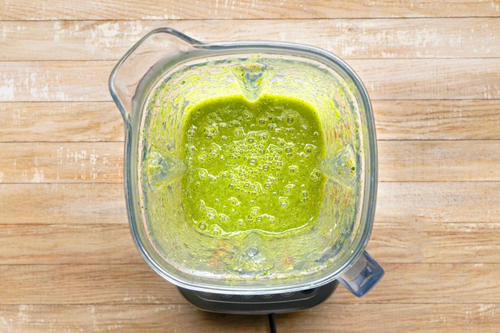overhead shot of a blender with a green smoothie inside, sitting on a wooden surface
