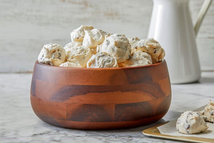 A wooden bowl filled with Forgotten Cookies, speckled with chocolate chips, rests on a marble surface