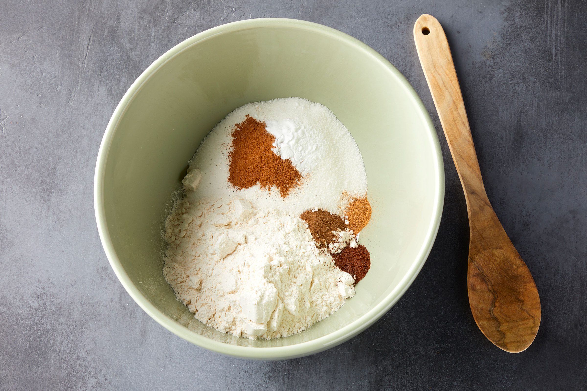Flour, sugar, spices and baking soda in a large bowl with a wooden ladle on side