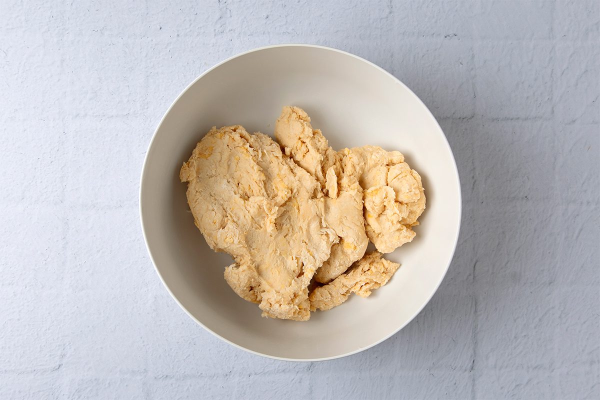 A white bowl filled with beige cookie dough sits on a light gray textured surface.