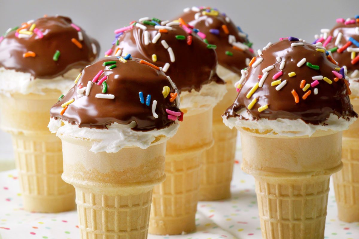horizontal shot of a tray of homemade ice cream cones dipped in chocolate and decorated with sprinkles; the cones are arranged on a tray with a colorful polka dot design
