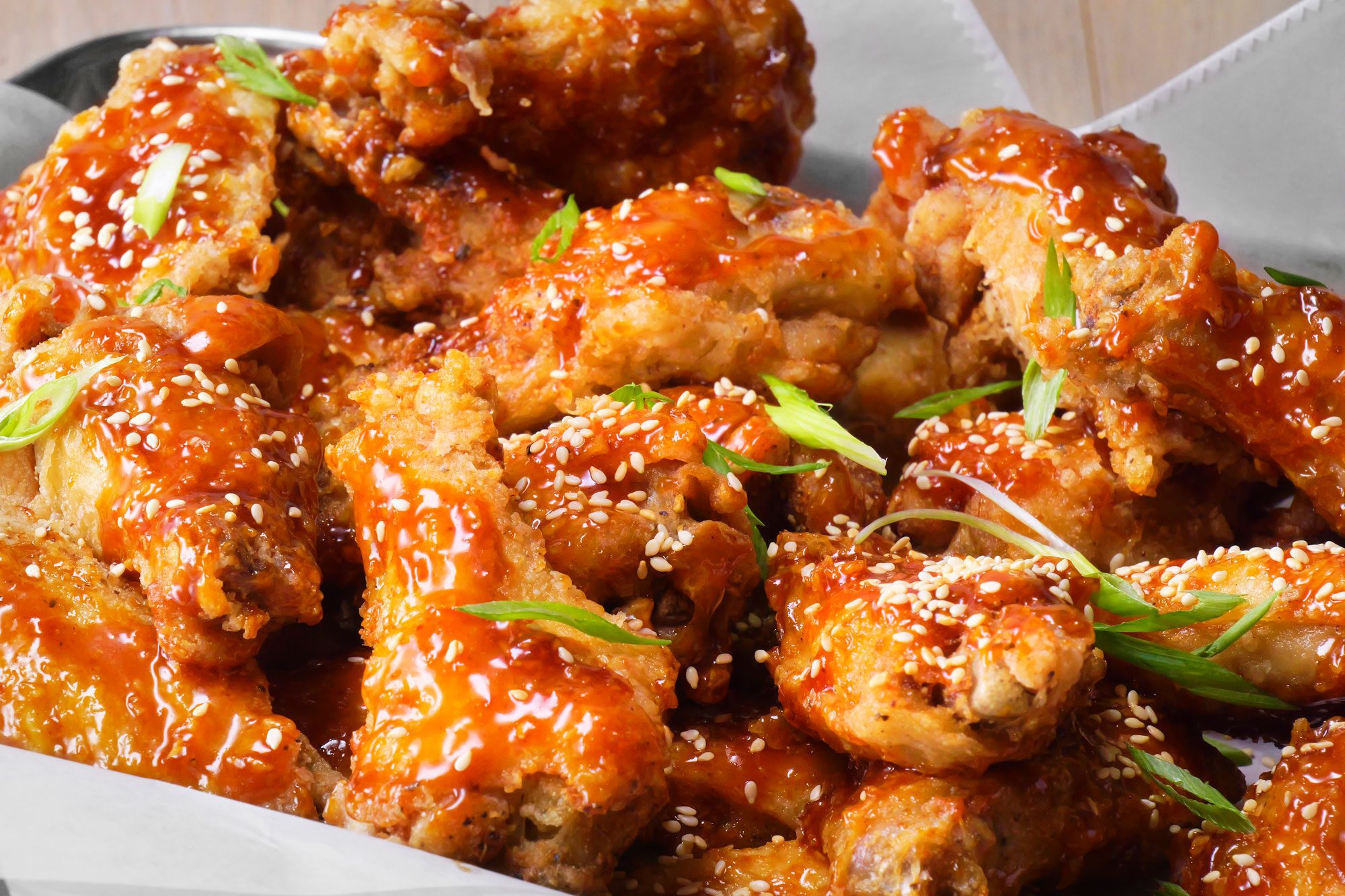 A plate of fried chicken wings coated in a sweet and spicy sauce and sprinkled with sesame seeds