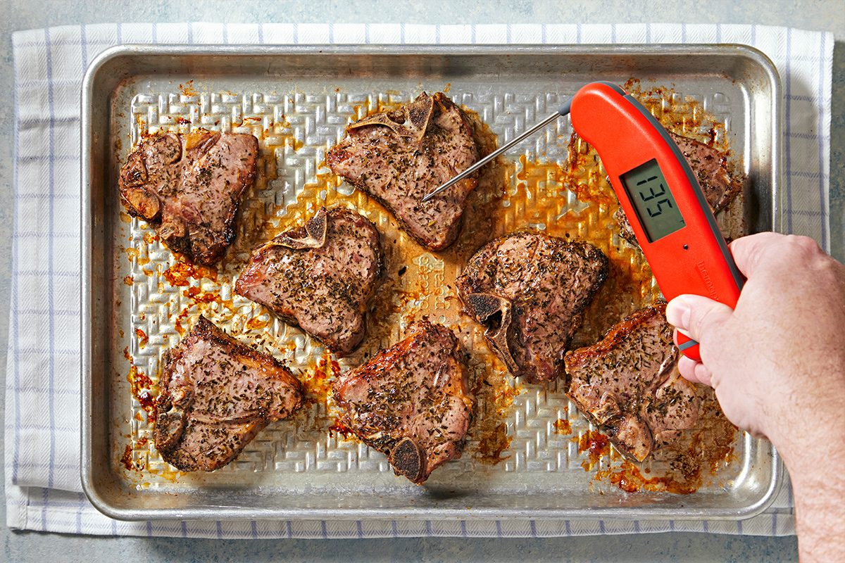 Overhead view of broiled lamb loin chops with a thermometer inserted in it reading 135°F kept on a baking tray on top of a kitchen cloth.