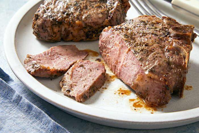 Side view of prepared and thinly cut slices of the cooked lamb loin chops on a white plate.