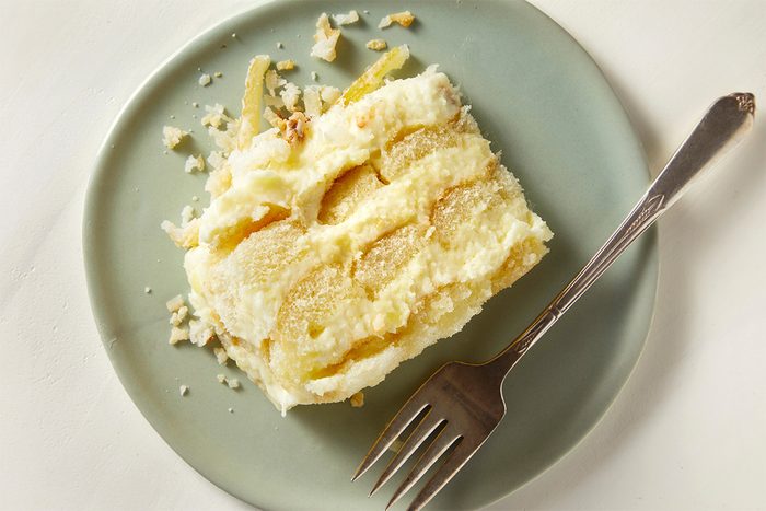 Sliced limoncello tiramisu top view plated and served with crumbled cookies and candied lemon peel on a green plate with a fork.