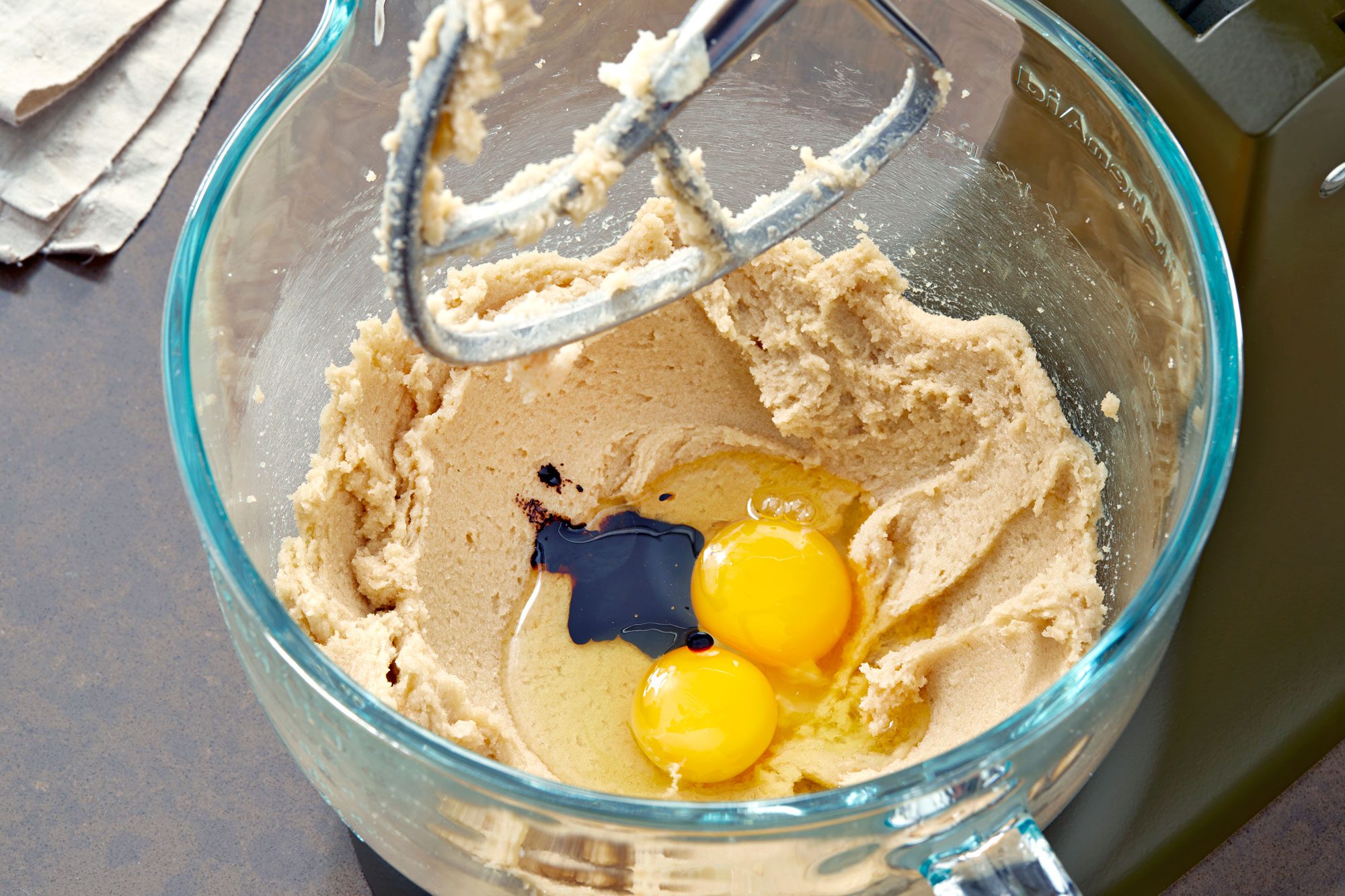3/4th view of a green bowl filled with white flour, baking soda, and salt; a whisk with a wooden handle is lying next to the bowl, partially out of frame; the ingredients are spread evenly in the bowl, with baking soda on the top left and salt on the bottom right