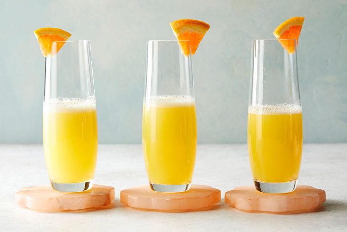 Table view shot of Mimosa; served in three glasses; garnished with orange slices; coaster; marble background;