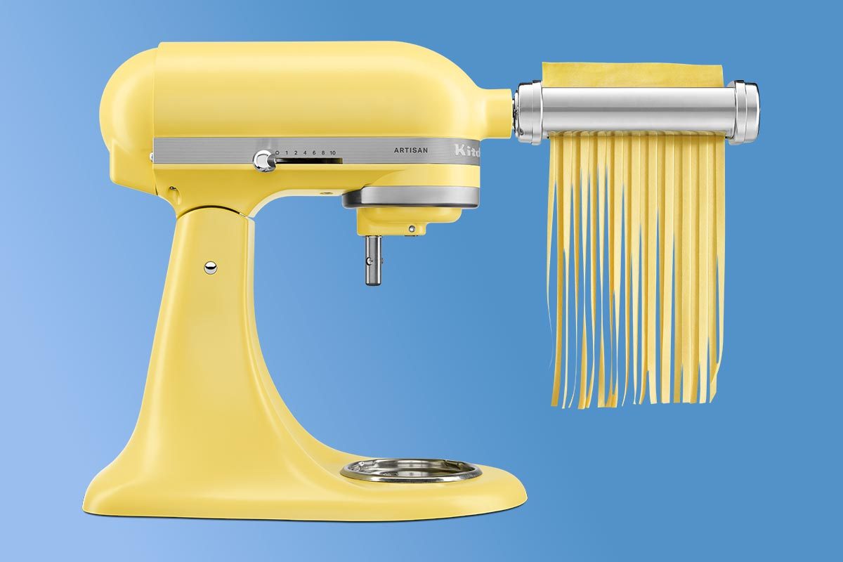 Kitchenaid stand mixer in a light yellow color with a pasta attachment cutting sheets of long pasta, on a blue background