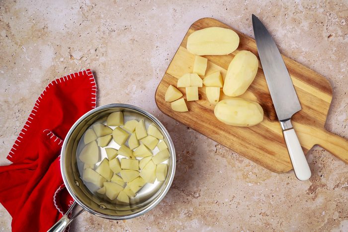 saucepan filled with water containing potatoes next to a chopping board with sliced potatoes and a knife