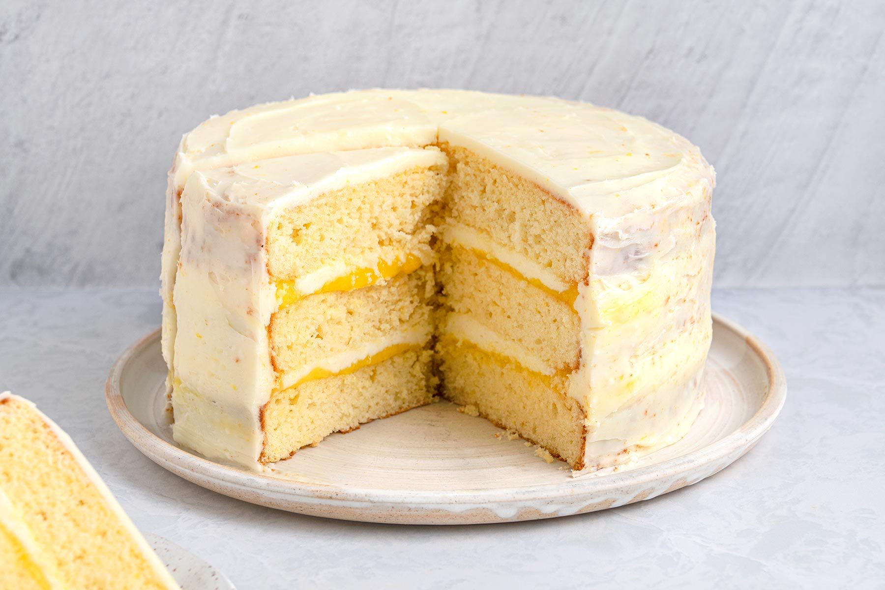 Wide shot of Lemon Curd cake with a slice taken out kept on top of a grey marbletop.