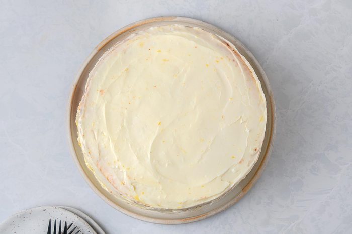 Evenly spread the frosting over cake kept on top of a grey marbletop.