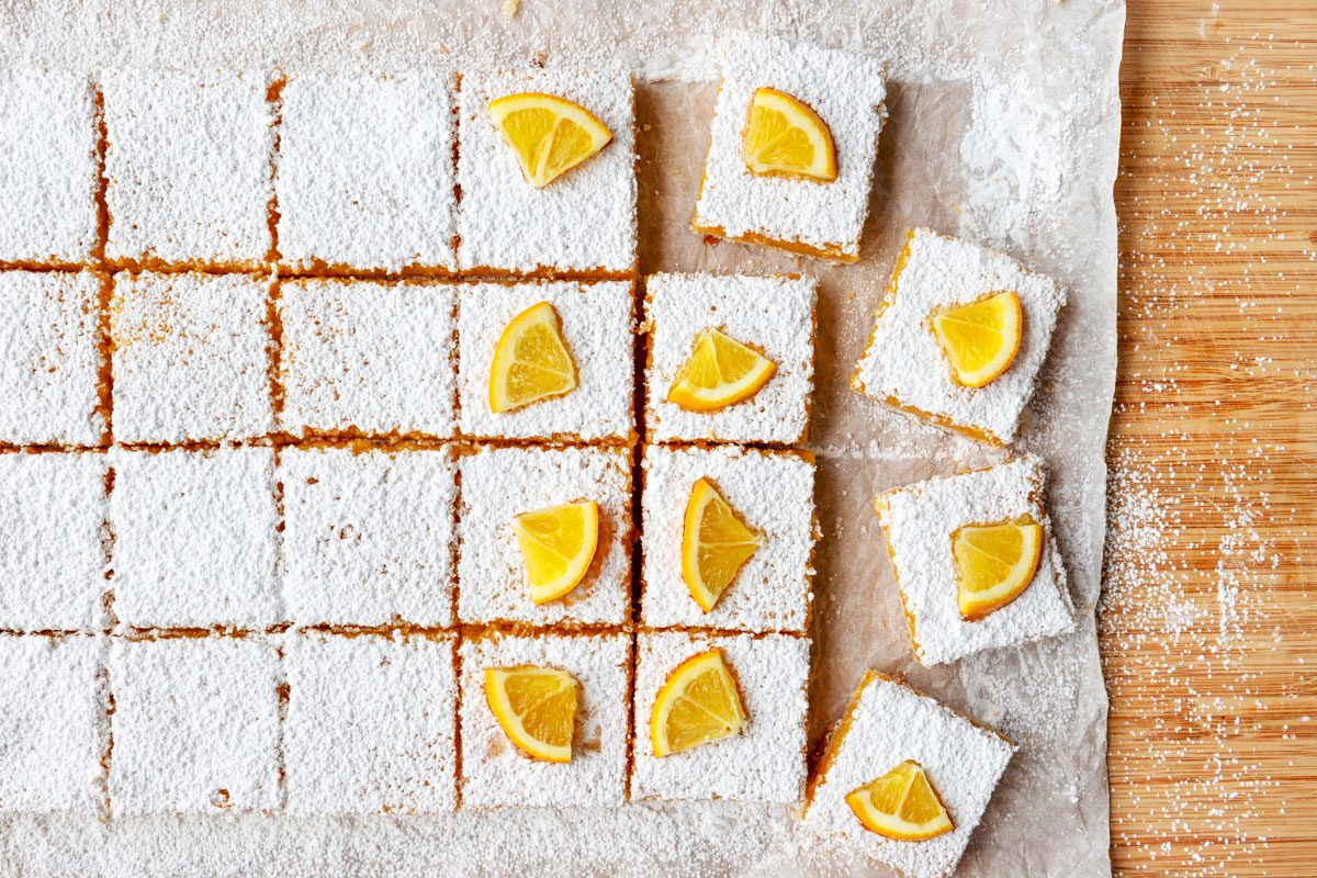 Meyer Lemon Bars being decorated and cut on a parchment paper covered surface