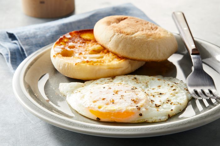 Close shot of Over-Easy Eggs; serve hot on a plate with bun and fork; over blue napkin; on grey surface;