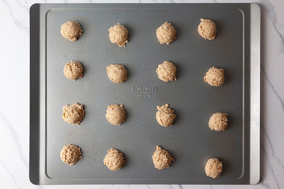 A baking tray with 15 evenly spaced unbaked cookie dough balls on a marble countertop.