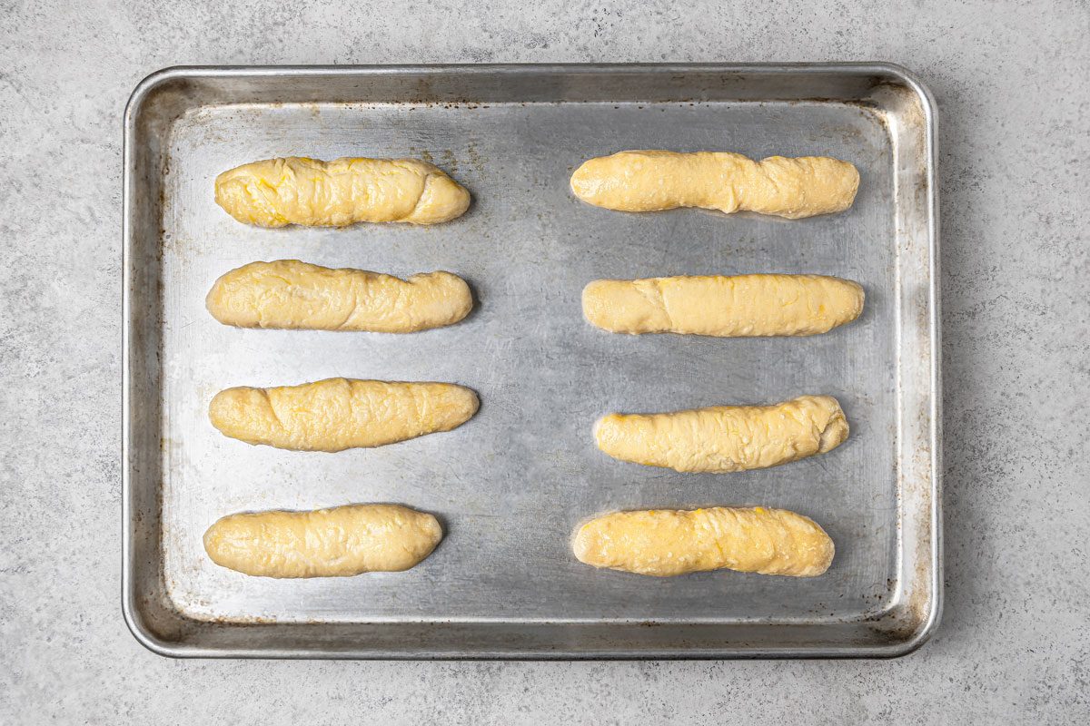 overhead shot of several uncooked pretzel sticks placed over grey metallic tray over light gray background