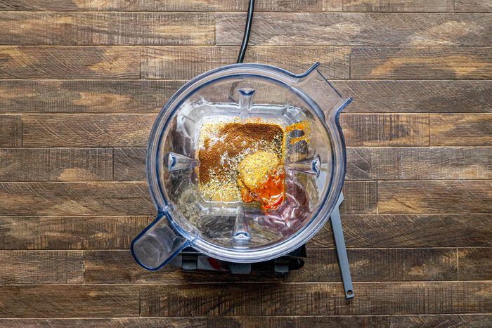 overhead shot of a blender on a wooden countertop; inside the blender is a mixture of spices