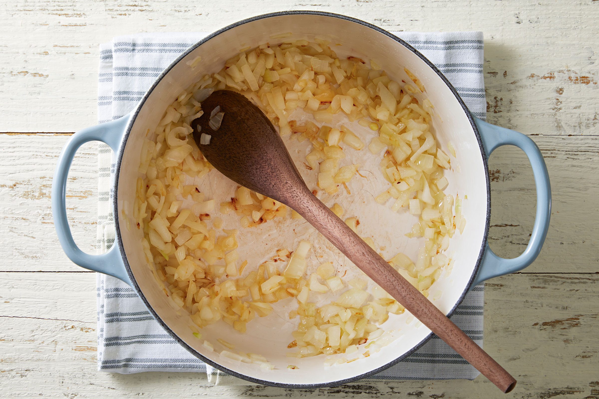 Onions cooking in oil in a Dutch oven with a wooden ladle on it