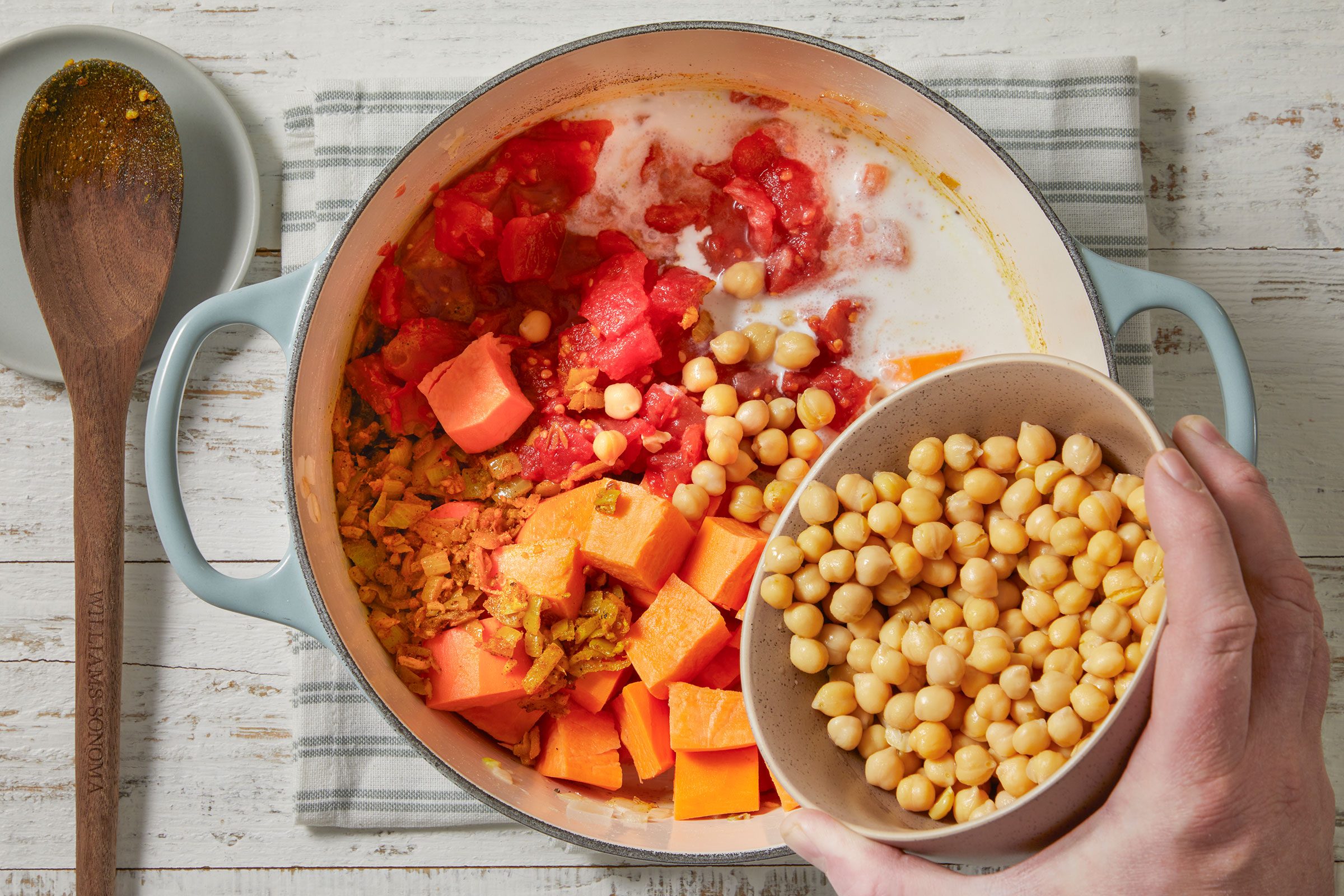 Sweet potatoes, broth, coconut milk, tomatoes with juice and garbanzo beans added to cooked onions in a Dutch oven