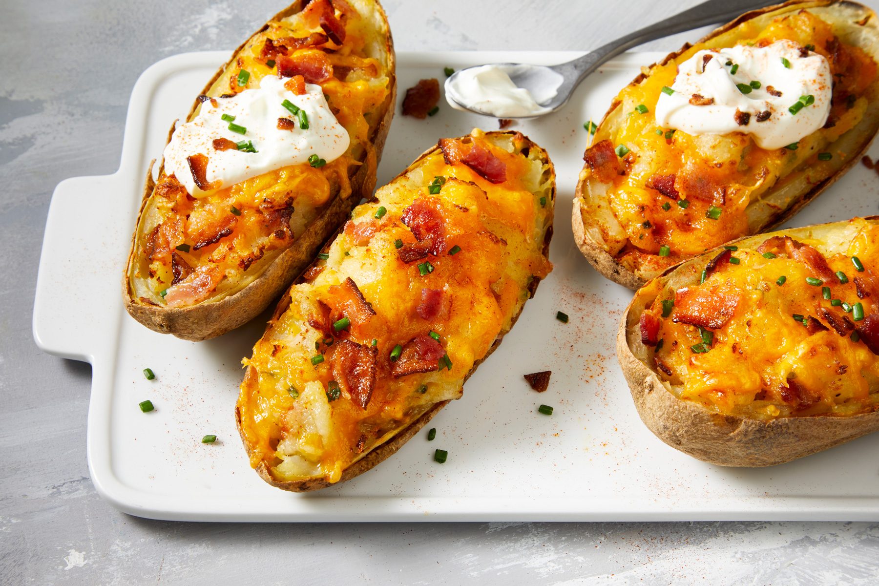 High angle shot of Air-Fryer Twice Baked Potatoes topped with additional bacon and chives, dollops of sour cream and a sprinkle of paprika.