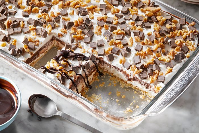 A glass dish holds a layered dessert with a corner piece missing, revealing layers of cream and chocolate.