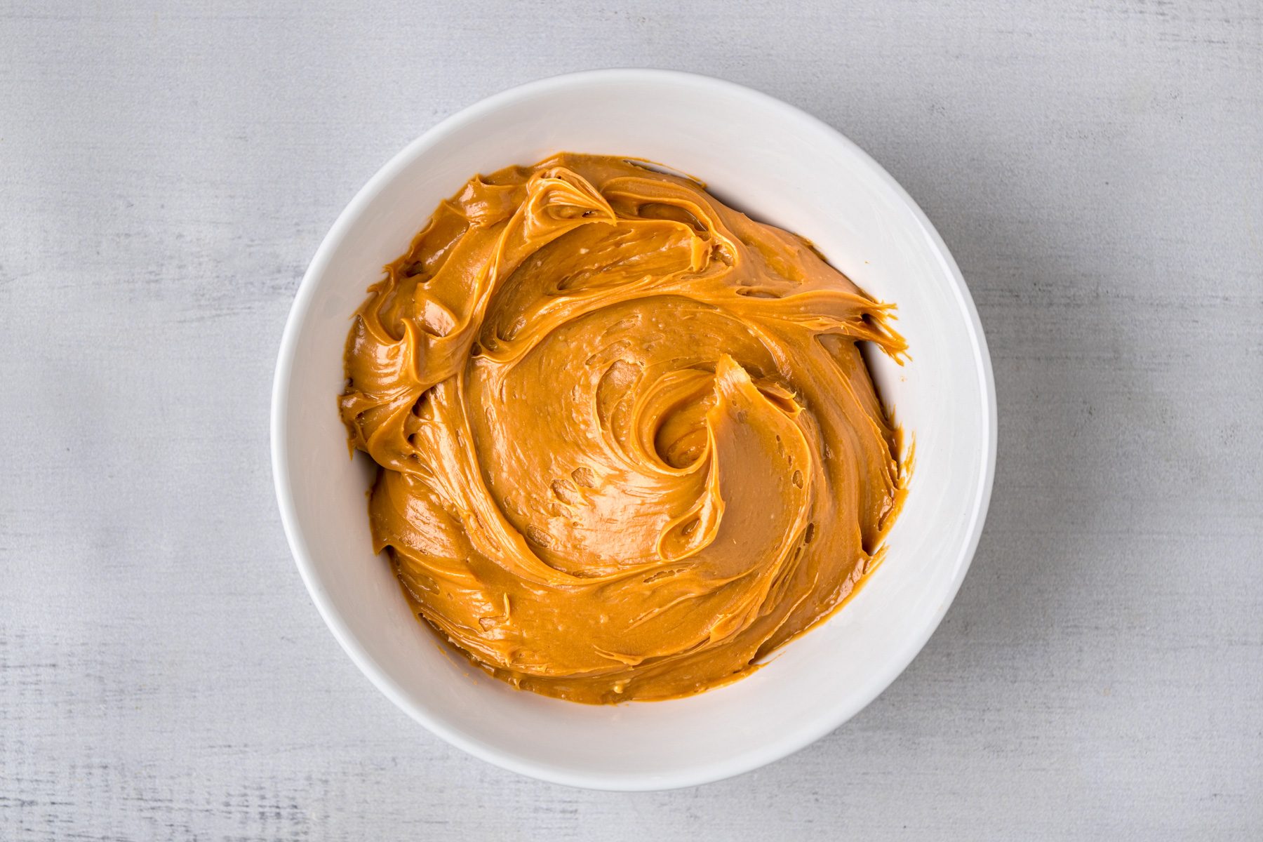overhead shot of a smooth and creamy spread, placed in a white circular bowl; the background is a light gray surface