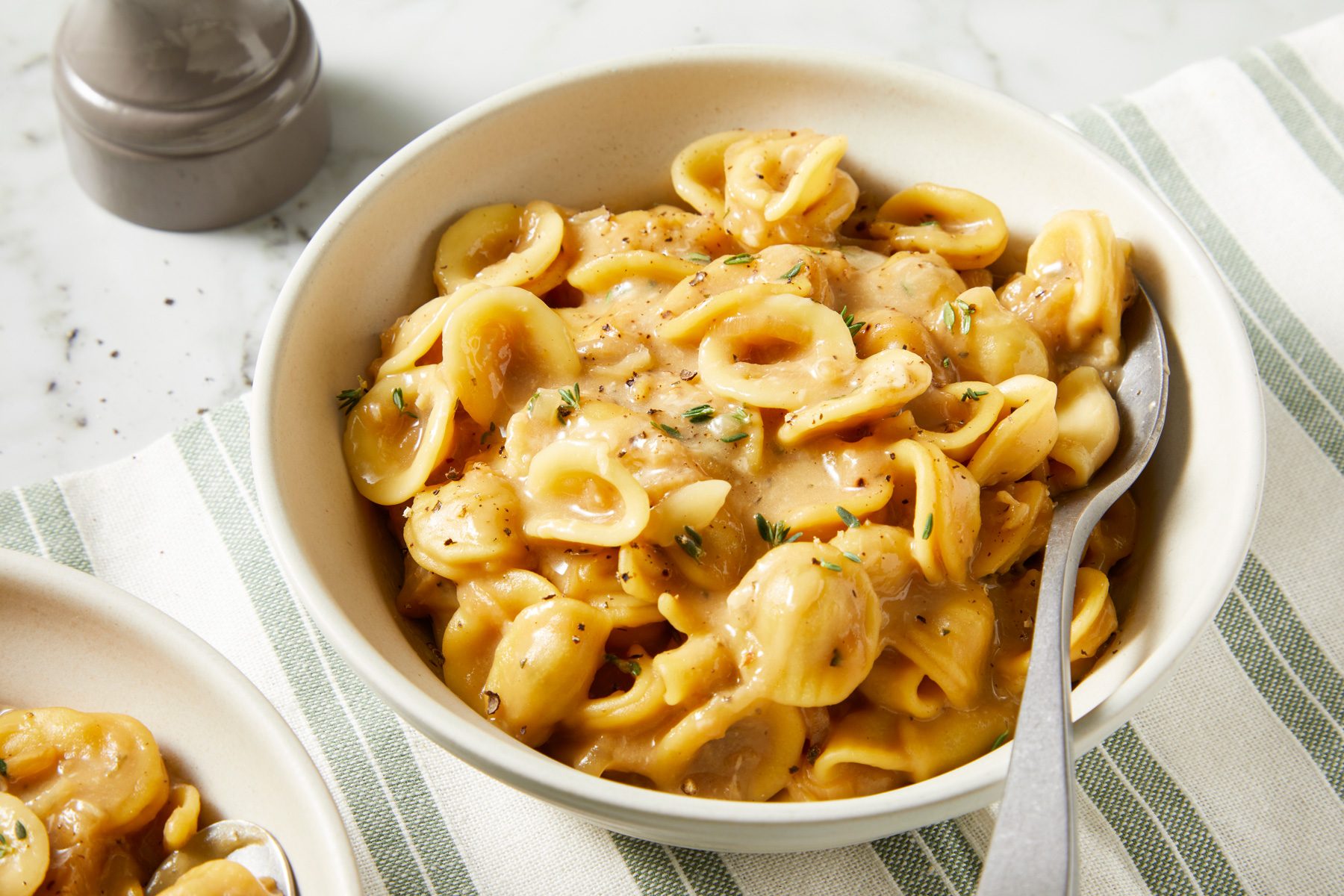 Pasta spooned into shallow bowls, garnished with shredded cheese and fresh thyme leaves, served hot.