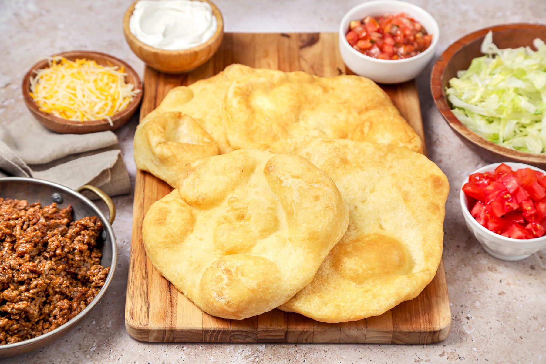 Dough fried and served on a wooden board with different taco toppings