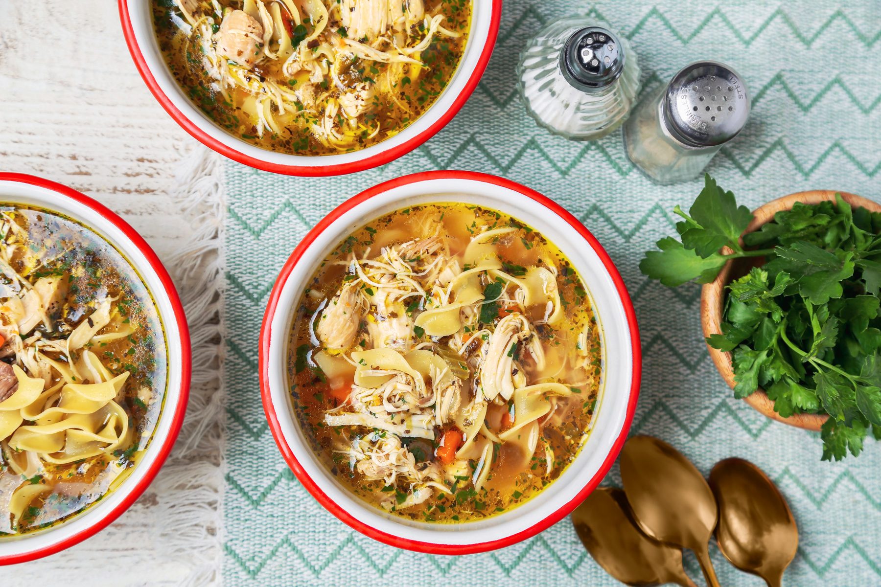 Cover push pull image of Taste of Home's Instant Pot Chicken Noodle Soup shot on a white wooden surface. Soup served in white and red enamel bowls with chopped fresh parsley as garnish; overhead