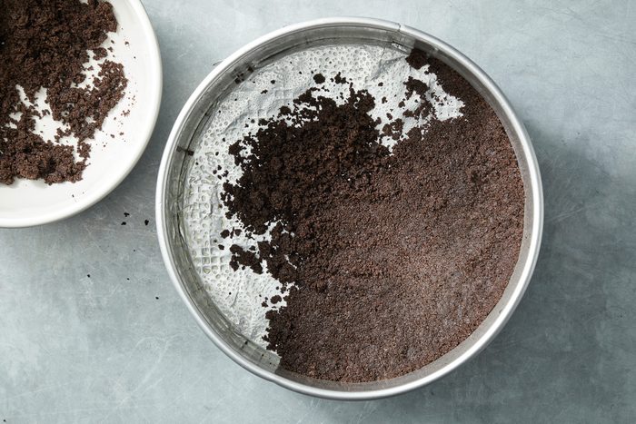 Overhead shot of press onto the bottom and 1 inch up the side of a greased 9-inch springform pan; all set on a grey surface;