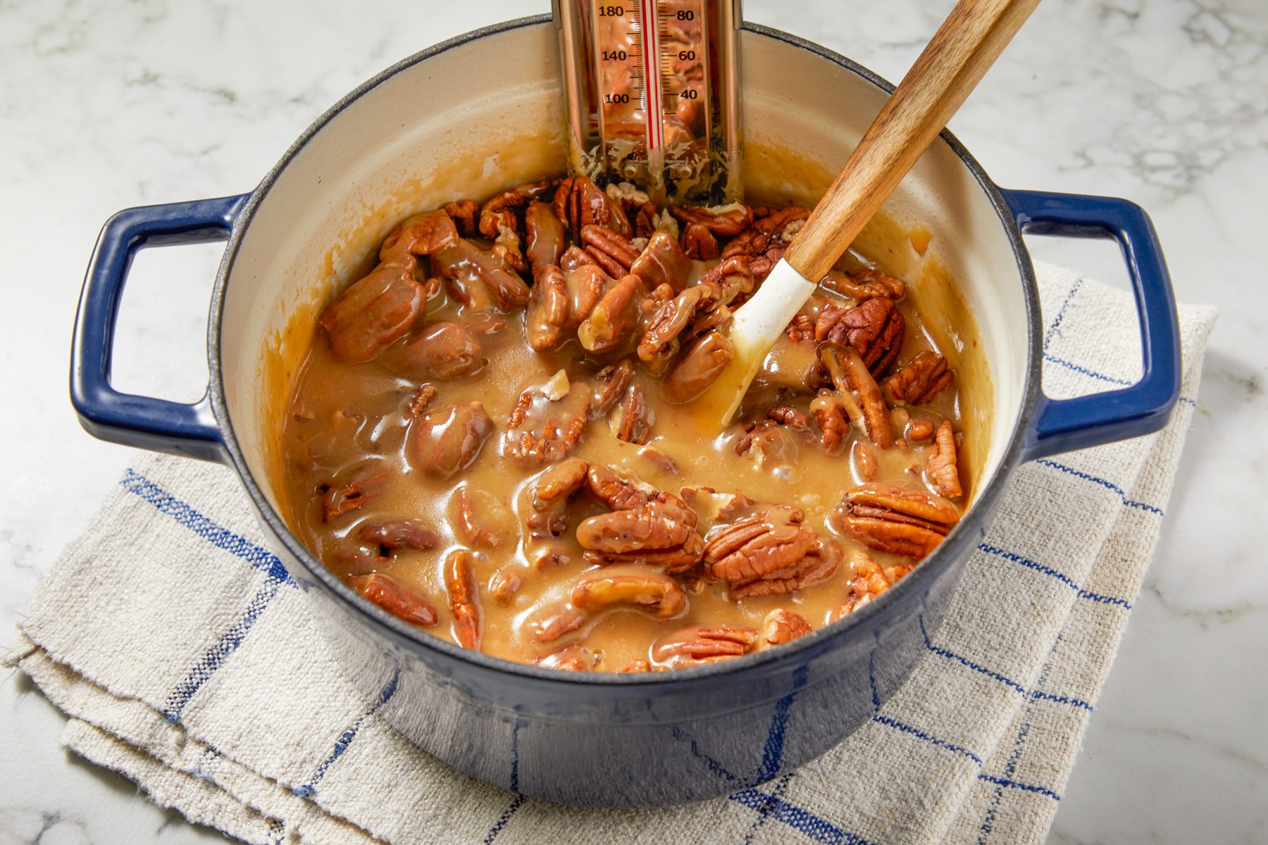 Overhead shot of remove from heat; stir in pecans and vanilla; Cool without stirring to 170 degree about 20 minutes; spatula; napkin; marble surface;