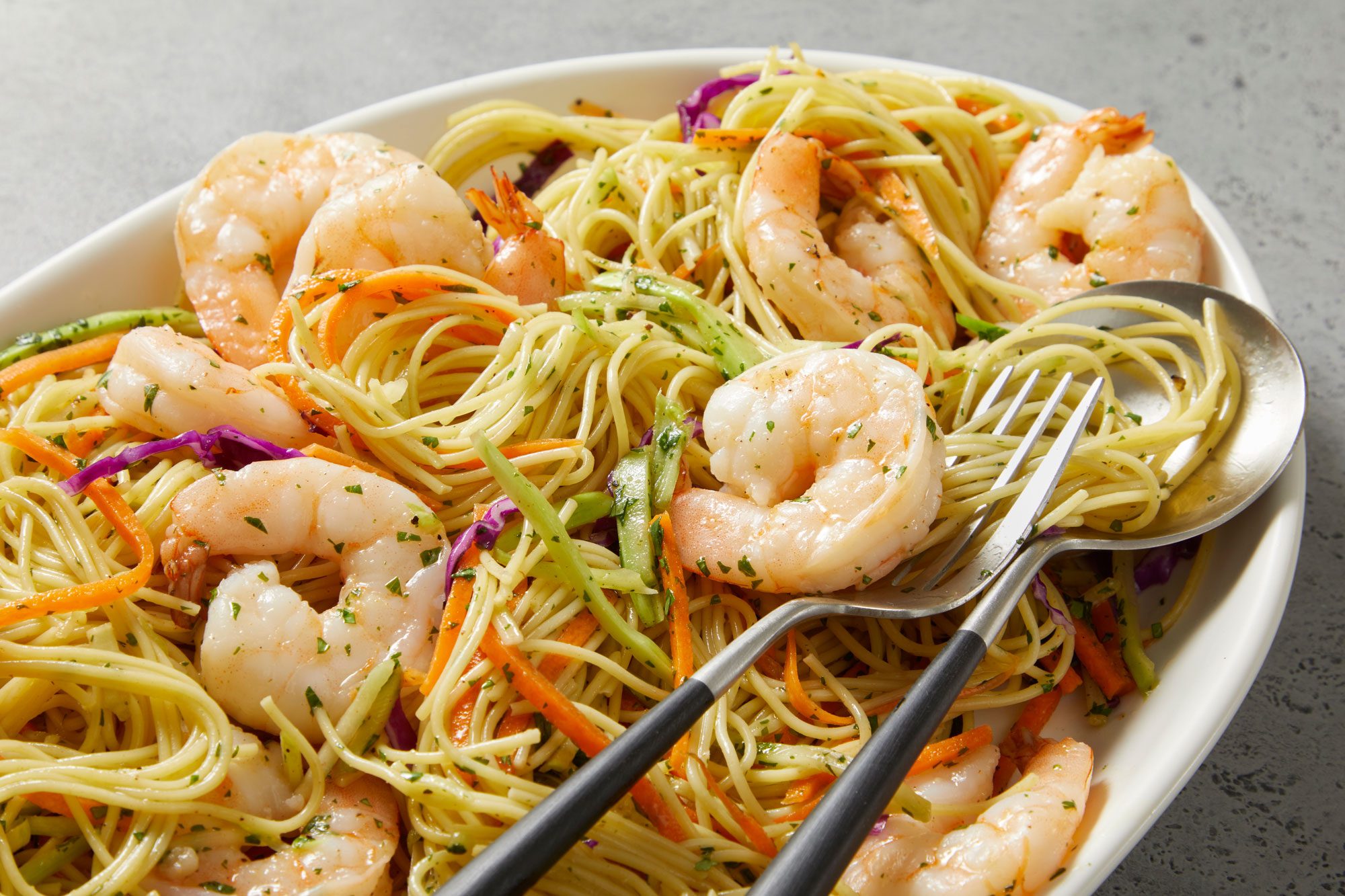 Close up shot of Shrimp and Noodle Bowls; served in a large bowl; Drizzle with dressing; fork and spoon; marble surface
